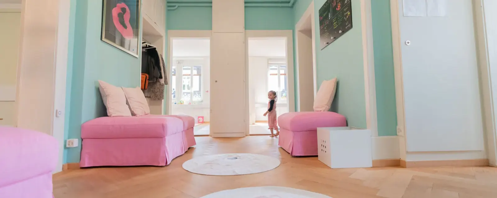 Blick in den Eingangsbereich der Kita Bärlis mit türkisen Wänden und rosa Sitzmöbeln